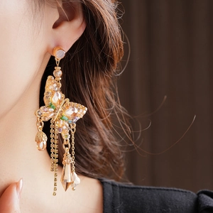 Gros plan de boucles d'oreilles papillon à pompons en cristal doré portées par un mannequin