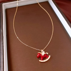 Close-up of a golden horse pendant with red enamel finish on a brown textured base