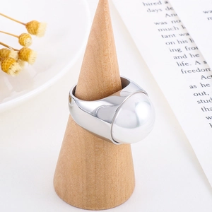 Détail d'une bague large en acier inoxydable avec grande perle blanche sur bois