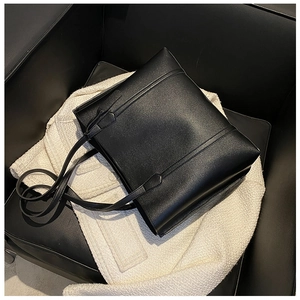 Close-up of a large black soft leather tote bag on a textured tweed surface and sofa
