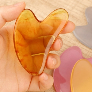 Close-up of heart-shaped amber resin gua sha tool with natural texture held in hand