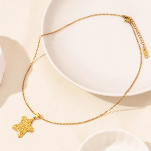 Detail of gold starfish pendant necklace with textured surface on a ceramic plate