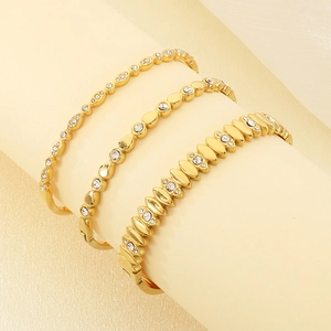Close-up of three 18K gold plated oval bangles with white zircon stones on beige props