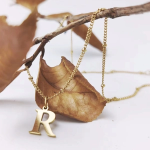 Detailed view of a gold-plated letter R pendant on a satellite bead chain necklace