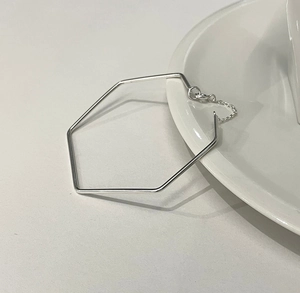 Close-up of a minimalist silver hexagon bangle with an adjustable chain on white ceramic