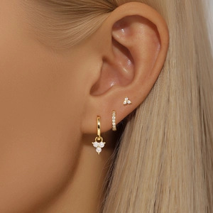 Macro shot of gold earring set with zircon-paved hoops and detachable three-diamond pendants