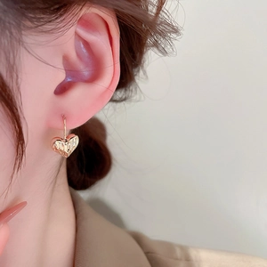 Close-up of a gold heart-shaped earring with wrinkled texture worn by a model