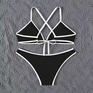 Flat lay of black and white bikini set with crisscross straps on textured fabric
