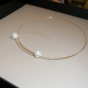 Macro detail of minimalist gold wire necklace with two lustrous white pearls on display
