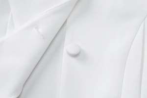 Close-up of white woven fabric with a matching fabric-covered button and buttonhole detail