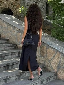 Detail of black textured handbag with metal B-buckle worn with sleeveless maxi dress