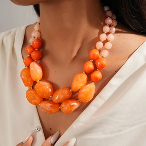 Close-up of double-layered orange and pink chunky resin bead necklace on white silk top