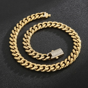 Macro detail of gold Cuban link chain necklace with diamond-set clasp on textured surface