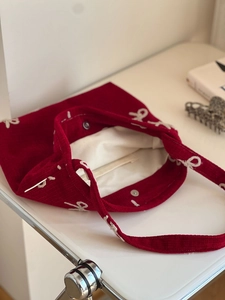 Detail of red corduroy shoulder bag with white bow pattern and metallic snap closure