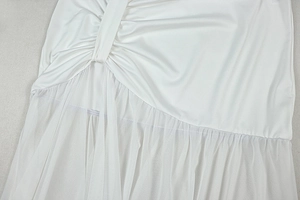Detail of white dress showing silky fabric texture with mesh splicing and pleated stitching