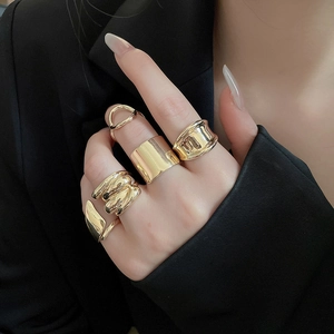 Detail of chunky gold geometric irregular rings worn by a model against a black suit