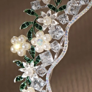 Close-up of bridal crown showing white pearls, green enamel leaves and crystals