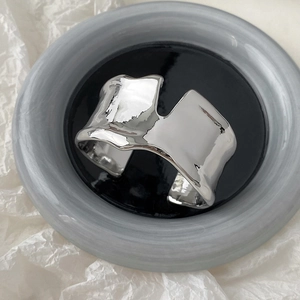 Gros plan du bracelet jonc ouvert argenté irrégulier avec texture de métal fondu sur plateau