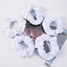 Detailed view of five white ruched fabric hair scrunchies arranged on a fashion magazine
