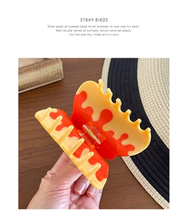 Detail of yellow and orange acetate hair claw clip showing metal spring and wing design