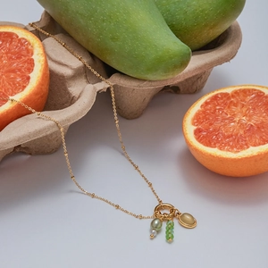 Dettaglio collana dorata con gemma a goccia verde e design con multi-pendenti