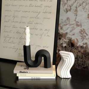 Modern black S-shaped ceramic candle holder with white decorative piece on art books