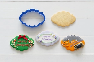 Blue scalloped plaque cookie cutter with festive icing decorations on white wood