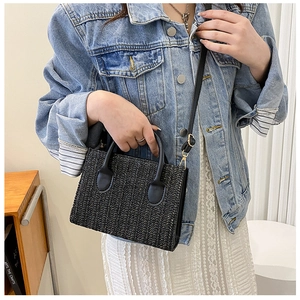 Close-up of black woven crossbody bag with leather handles and gold-tone hardware