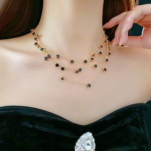 Détail d'un collier doré multicouche avec pierres noires rondes porté par un mannequin