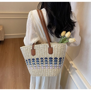 Detail of woven straw tote bag with blue gradient pattern and brown leather straps