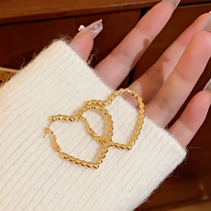 Detail of golden heart-shaped hoop earrings with textured wavy patterns held by hand