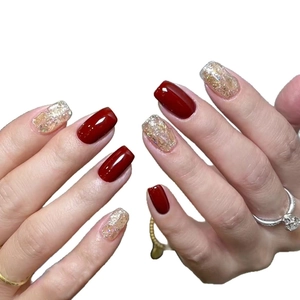 Short square press-on nails with dark red finish and gold glitter accents on hand model