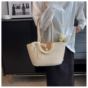 Detail of straw tote bag featuring white weaving, brown flap, and pearl buckle decoration