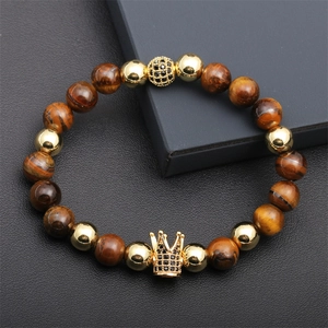 Macro shot of tiger eye beads and golden crown charm on a black leather texture background