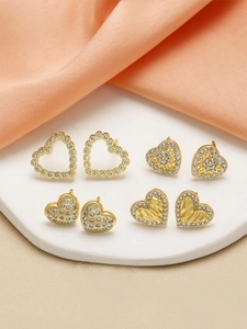 Close-up of four heart-shaped gold earrings with zircons on silk fabric