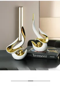 Détail de statues de cygne en céramique blanc et or sur un bureau noir élégant avec livres