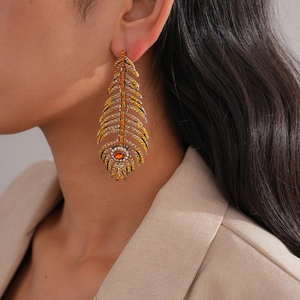 Boucles d'oreilles plumes dorées avec strass ambre et blanc portées par mannequin