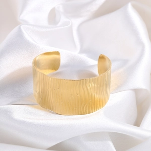 Detailed close-up of a wide gold adjustable cuff bracelet with leaf-like wavy texture