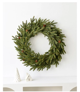 Close-up of artificial green Christmas wreath with pine cones against white background
