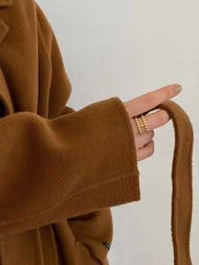 Primo piano di un anello a doppia fila di perline dorate a forma di H indossato da una modella