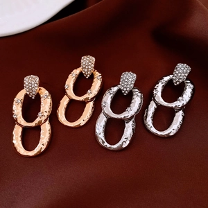 Close-up of gold and silver oval drop earrings with textured finish and sparkling rhinestones