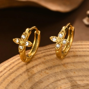 Close-up of golden hoop earrings with zircon flower studs on a rustic wooden base