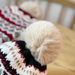 Close-up of white plush pom-pom and geometric jacquard knit fabric on earflap hat