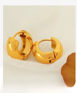 Close-up of chunky gold-plated stainless steel hoop earrings on white textured fabric