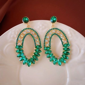 Boucles d'oreilles ovales vintage dorées avec cristaux verts et strass sur plat blanc