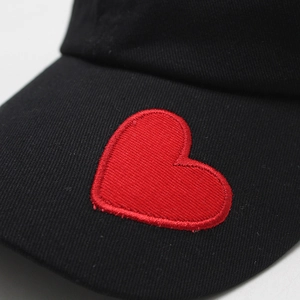 Dettaglio del ricamo a cuore rosso su cappellino da baseball nero in cotone lavato