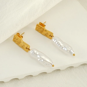 Détail de boucles d'oreilles dorées martelées avec perles baroques sur tissu blanc texturé
