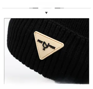 Detail of black ribbed knit beanie featuring a triangular beige rubber logo patch