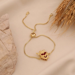 Adjustable golden Sacred Heart charm bracelet with red enamel on a warm natural background