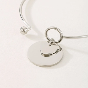 Close-up of polished stainless steel bangle with heart and round charms on leather surface
